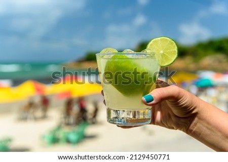 Drink caipirinha. Hand holding a caipirinha drink on a beach in Brazil with a blurred background. Royalty-Free Stock Photo #2129450771