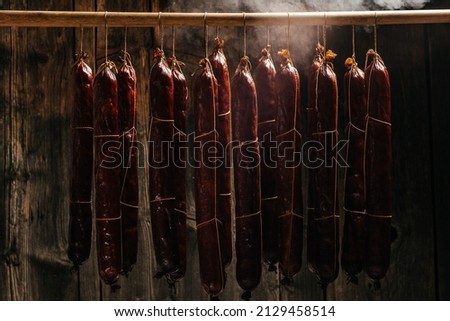 Process of smoking sausage hang in a cupboard with smoke. Clouds of smoke rise up and envelop the sausages hanging in a row. Long banner format,