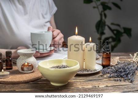 Woman is reading a book and drinking tea in atmosphere of harmony and relaxation. Aroma lamp with essential oils and burning candles on the wooden table. Royalty-Free Stock Photo #2129469197