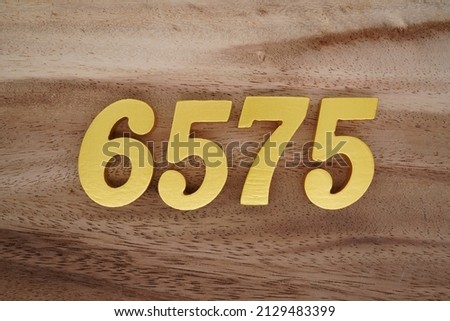 Wooden  numerals 6575 painted in gold on a dark brown and white patterned plank background.
