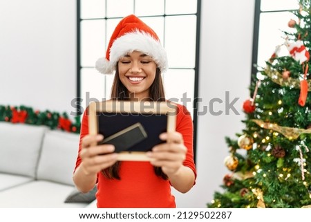Young latin woman looking photo standing by christmas tree at home