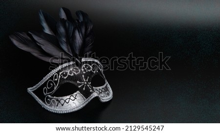 Black and silver carnival mask with black feathers on black background with green graphic glitter. Design for Purim, Mardi Gras celebration with copy space