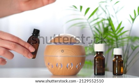 Modern aroma oil diffuser on the white table. Spa concept for body and health care. female is adding essential oil to an aroma diffuser. Royalty-Free Stock Photo #2129552510