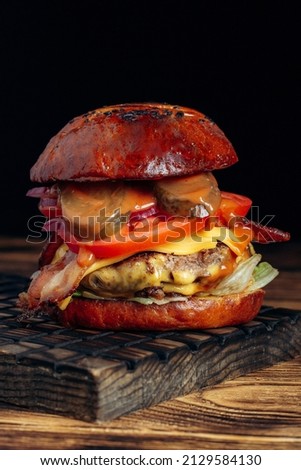 Burger with cheese, meat, vegetables on a wooden tabletop.