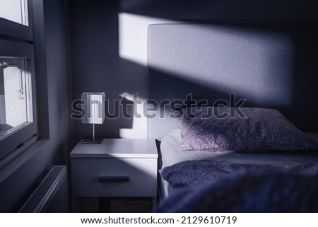 Bed at night in dark bedroom. Blue light and moonlight from window. Pillow, sheet and duvet ready for sleeping. Bedside table and nightstand. Scandinavian home interior design. Scary shade and shadow. Royalty-Free Stock Photo #2129610719