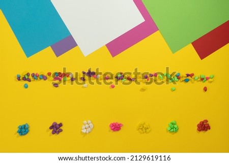 Fluorescent pebbles arranged in several ways on a yellow background. Neon colors paper in the upper part. Minimalist concept of creative design. Flat lay.