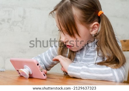 little girl at the table playing on the phone watching a video