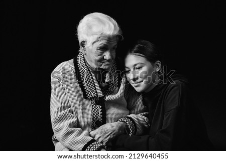 Elderly woman sitting with an adult granddaughter a black background. Black and white photo.