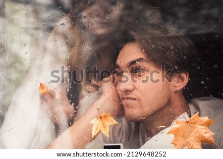 Sad unhappy lovers couple behind wet misted window,rain drops.Drawing heart with finger.Autumn atmosphere,mood,maple leaves.Love romantic road travel. Traveling in camper,house on wheels,trailer.
