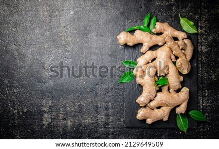 Fresh ginger with leaves on a stone board. On a black background. High quality photo