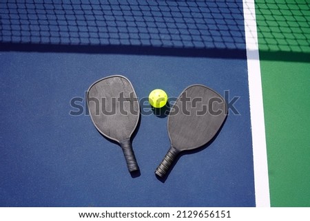 Pickle ball paddle and pickle ball on court with net shadow in background. Royalty-Free Stock Photo #2129656151