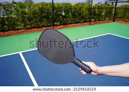 Person holding pickle ball paddle on court.                       Royalty-Free Stock Photo #2129656559