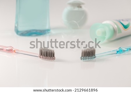 Two toothbrushes laid on a white table and in the background mouthwash, interdental floss and toothpaste.