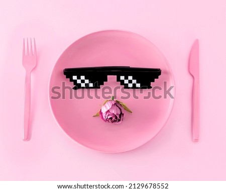 Creative look with a pastel pink plate, fork, knife, retro pixel glasses from the 80s and 90s and spring flowers on a pink background. The concept of a restaurant with aesthetic fashion food.