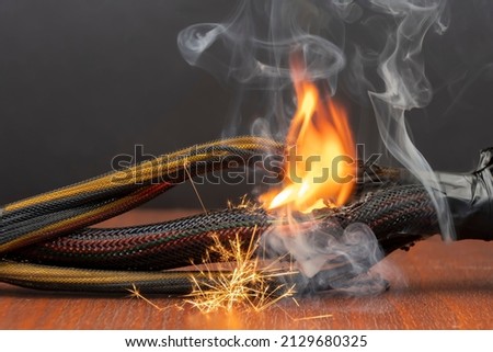 The wiring is burning and sparking on a dark background. A short circuit in the twisted wires from the computer. Flames, sparks and smoke. Royalty-Free Stock Photo #2129680325