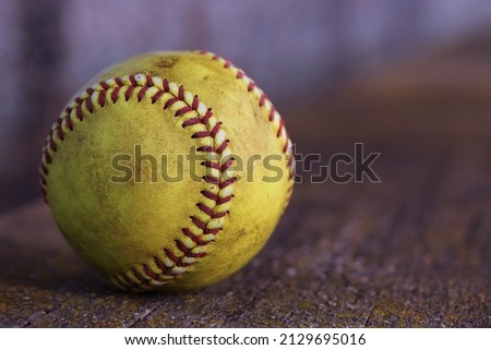 A yellow softball sits on a wooden bench.