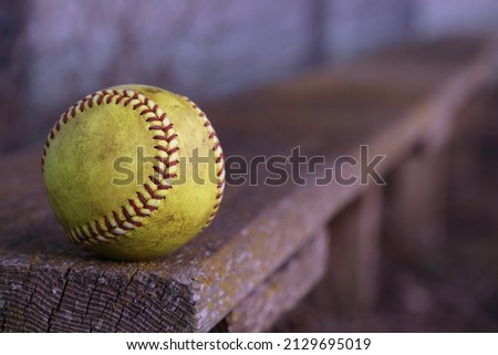 A yellow softball sits on a wooden bench.