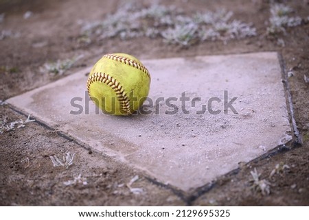 A yellow softball rests on a home plate.