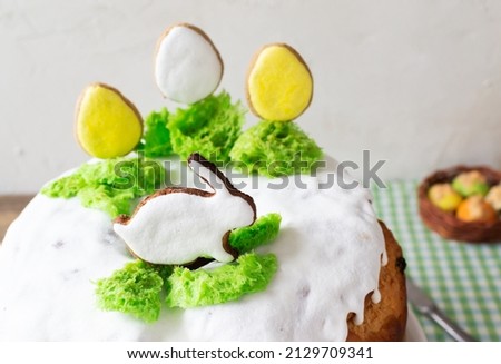 Easter cake with raisins decorated with white icing and gingerbread in the shape of Easter eggs and a rabbit on green grass on a green checkered tablecloth. Rustic