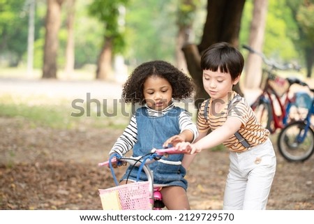 Love boy bother teaching her cute sister to ride a bicycle. Both smiling and looking at each other. Summer park in background