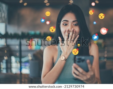 A beautiful woman looks at her smartphone in amazement against 
When receiving emoji and emoticon reactions on her mobile smart device while posting. Social media ideas and marketing sharing or video  Royalty-Free Stock Photo #2129730974