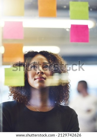 Thinking critically to create success. Shot of a young woman having a brainstorming session with sticky notes at work. Royalty-Free Stock Photo #2129742626