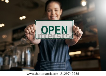 I took a risk in opening my dream coffee shop. Portrait of a young woman holding up an open sign in her store.