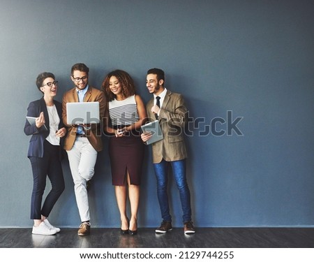 The connected team is an efficient team. Studio shot of a group of businesspeople using wireless technology together while standing in line against a gray background. Royalty-Free Stock Photo #2129744255