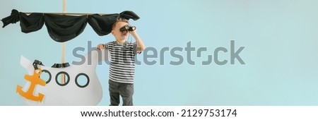 Little child boy playing with cardboard ship on blue wall background