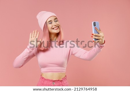Young woman 20s with bright dyed rose hair in rosy top shirt hat doing selfie shot on mobile cell phone waving hand isolated on plain light pastel pink background. People lifestyle fashion concept.