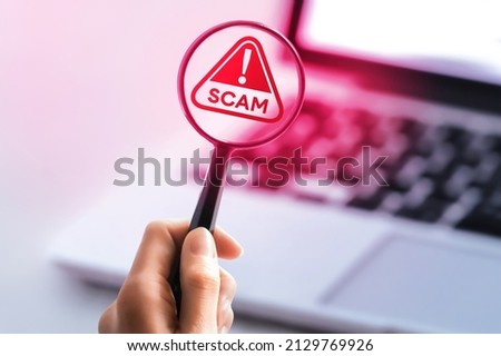 Person hand holding a magnifying glass pointing at the screen of notebook. Internet search concept. Red scam buttons and magnifying glass. Royalty-Free Stock Photo #2129769926