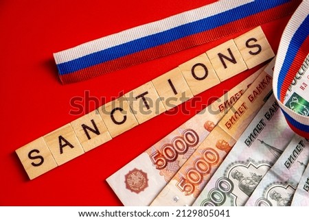 Russian ruble banknotes issued by the Bank of Russia on red background with Russian flag ribbon. Russian ruble under sanctions. Royalty-Free Stock Photo #2129805041