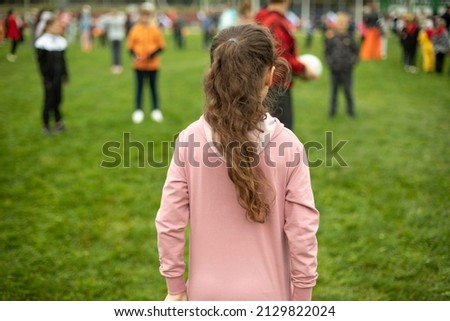 Child does exercises in fresh air. Sports activity for schoolchildren. Children on green grass. Playing in park. Schoolgirl stands with her back.
