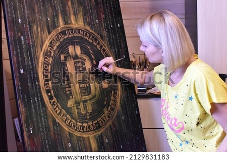 Woman artist draws a large picture with paints in  studio. hobby painting with oil paints on canvas. artist draws bitcoin