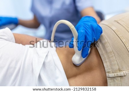 young female doctor examining kidney of patient with ultrasound scan. Close up photo of lower back of young woman getting ultrasound test in clinic. Hand of a doctor holding ultrasound scanner.
