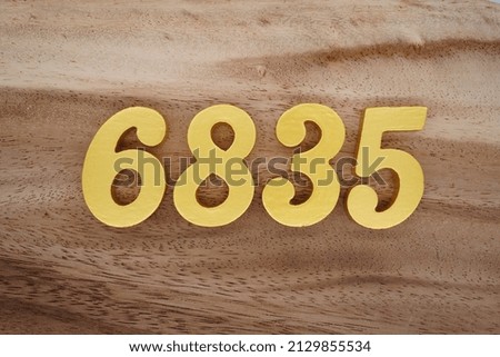 Wooden  numerals 6835 painted in gold on a dark brown and white patterned plank background.
