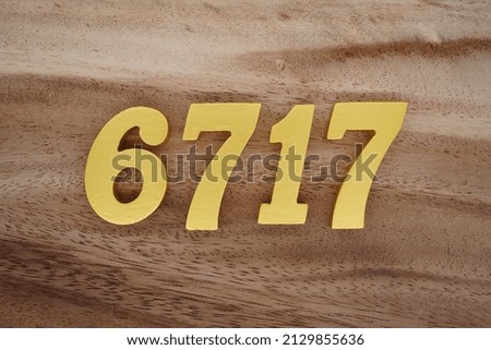 Wooden  numerals 6717 painted in gold on a dark brown and white patterned plank background.