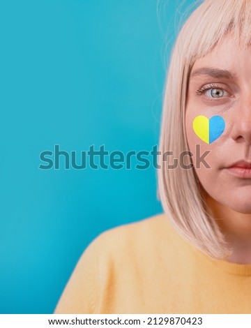 Sad woman face with love symbol blue yellow ua national colors looking at the camera isolated on dark blue background.