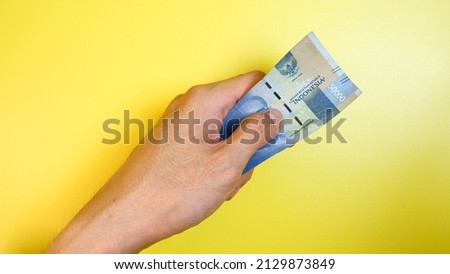 Indonesian Rupiah the official currency of Indonesia. A man's hand is making a payment. Male hand showing Indonesian Rupiah note. Business Investment Economy and Finance concept. Uang 50000 Rupiah.