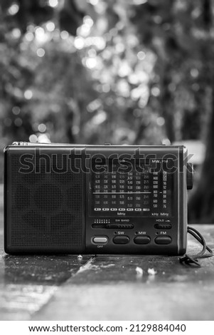 an analog radio on a gardenoutdoor wooden table against a blurred background of trees. photo in black and white for an old school impression