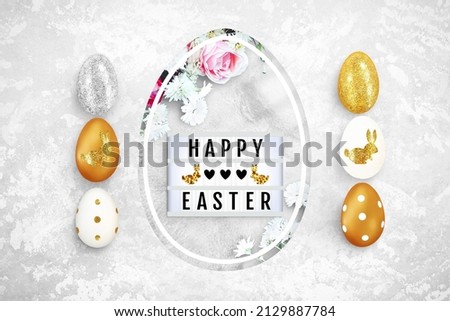 Shining Easter eggs on a concrete background. Lightbox and flowers in egg shaped hole. Text frame of the lightbox with the inscription Happy Easter, hearts, bunnies. Top view, close up, copy space