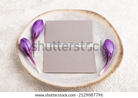 Gray paper invitation card, mockup with crocus flowers on ceramic plate and gray concrete background. Blank, flat lay, top view, still life, copy space, wedding invitation.