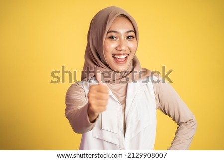 woman in hijab smiling with thumbs up while standing