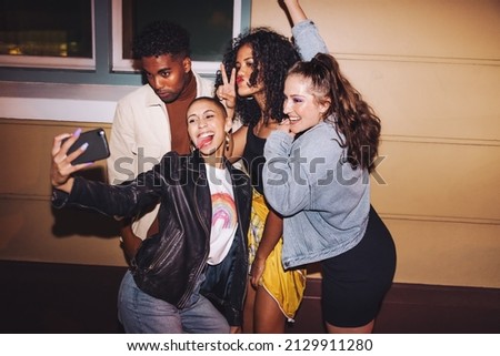 Time for crazy night selfies. Group of multicultural friends taking a group photo together while standing outdoors at night. Vibrant young people having a good time on the weekend.
