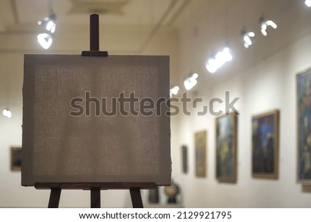 An empty painting canvas on the wooden easel with blurred gallery background, selective focus