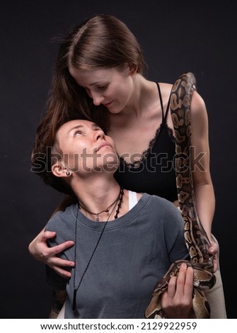Photo of two hugging women with snake on shoulders