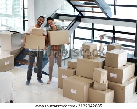 Starting a new life together in a new home. Portrait of a happy young couple carrying boxes while moving into their new home.