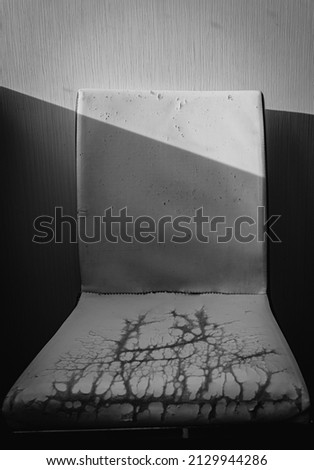 Sunny room with old kitchen chair on wall pattern background. Shabby white chair in heavy used condition with worn fabric and scratch. Broken and damage furniture, need repair or change. BW picture.