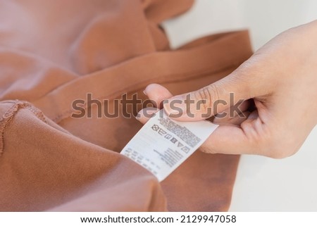 Housewife, asian young woman hand in holding shirt label, tag with instructions, guide before clean clothes, fabric into washing, drying machine, making household working at home. Laundry and maid. Royalty-Free Stock Photo #2129947058
