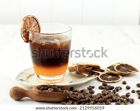 Layered non-alcoholic cocktail recipe idea. Orange juice in the bottom and dark coffee on the top in the glass. Bright and cozy still life of coffee beans, orange slices and layered cocktail.